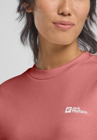 Top a maniche corte, collo rotondo in morbido tessuto rosa con logo bianco sul lato sinistro del petto. Texture liscia e design aderente.