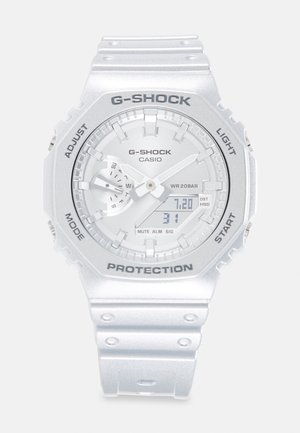 Hvid Casio G-Shock-ur med analoge visere, digital dato- og ugedagsvisning samt mærkede knapper til justering, tilstand, lys og start.