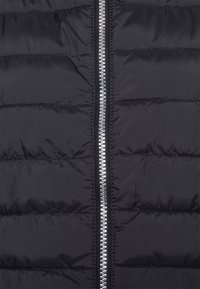 Veste doudoune noire avec une fermeture éclair argentée brillante, texture matelassée avec des coutures horizontales, et tissu lisse et réfléchissant.