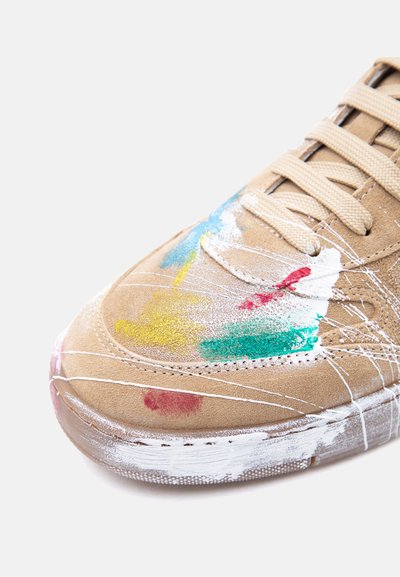 Zapatilla de gamuza beige con salpicaduras de pintura multicolor y rayas de pintura blanca en la puntera y la suela, cordones beige atados.