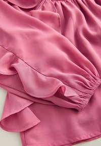 Rosa Bluse aus leichtem Stoff, mit Rüschenschultern und einem elastischen Taillenbund, in glatter Textur und fließendem Design.