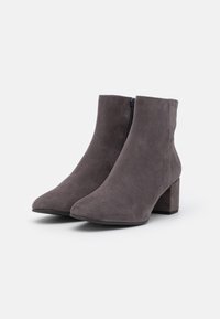 Šedé semišové kotníkové boty s špičatou špičkou a masivním podpatkem, s bočním zipem pro snadné obouvání. Hladká textura a minimalistický design.