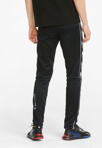 Černé sportovní kalhoty s úzkým střihem, se zkušenostmi v podobě bílých bočních pruhů a detailů s logem. V páru s černými a červenými sportovními botami.