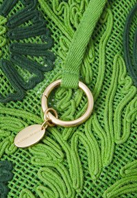 Zielony tkaninowy materiał z misternym haftem w różnych odcieniach zieleni. Posiada złoty pierścień i metkę z wygrawerowanym napisem "Vanessa Bruno".