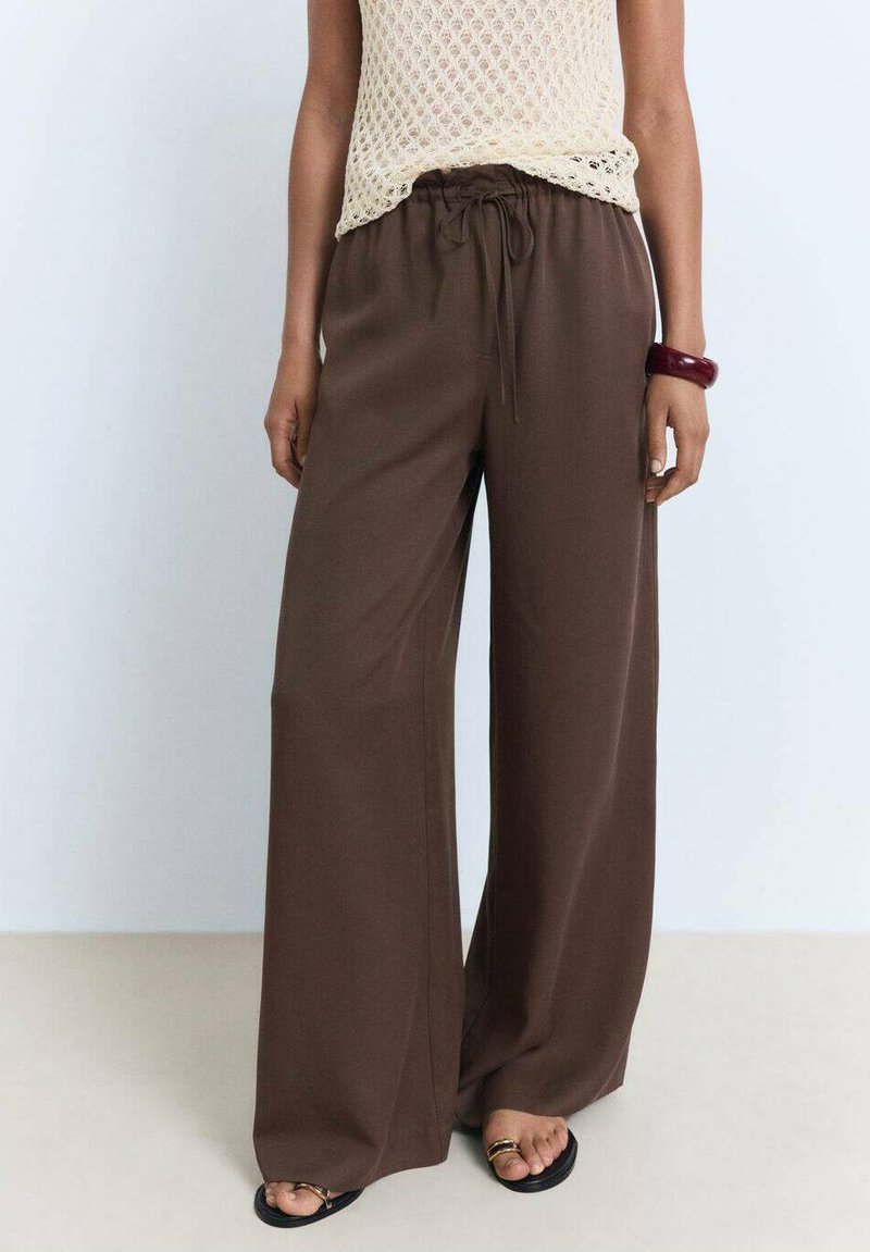 Pantalons larges marron avec une taille à cordon, en tissu doux. Associés à un haut en crochet léger et des sandales noires minimalistes.