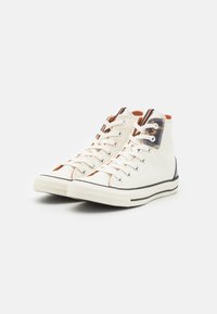 Sneaker alte in tela off-white con accenti beige, suole in gomma nere e occhielli metallici. Presentano tasselli di colore contrastante sui lati.