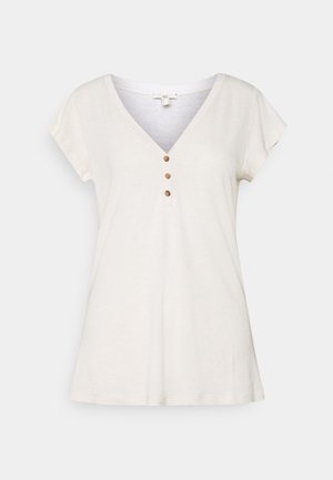 T-shirt à manches courtes et col en V en coton beige clair avec quatre petits boutons en bois au niveau du col et une coupe décontractée. Texture douce.