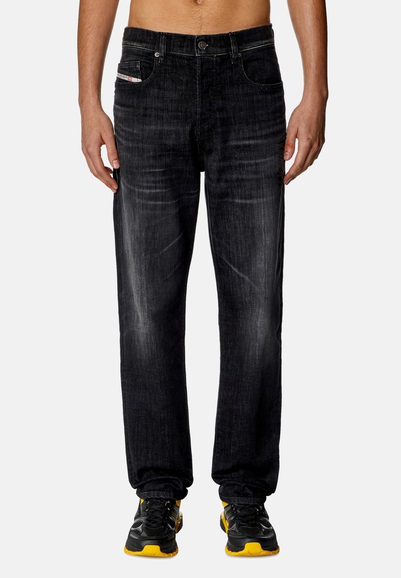 Pantalones vaqueros negros de mezclilla con corte recto, decoloración sutil, cinco bolsillos y un detalle de cinturilla en contraste. Combinados con zapatillas negras y amarillas.