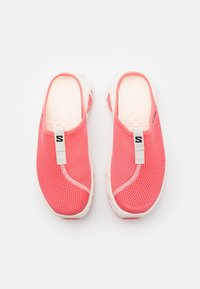 Des baskets corail vives à enfiler, présentant une tige en mesh, une semelle blanche et un design minimaliste avec un détail de tirette contrasté. La texture est respirante.