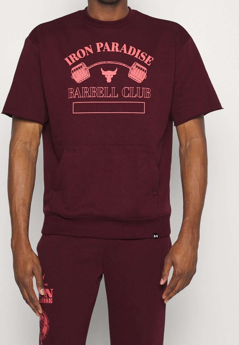 Sudadera corta de manga corta en color burdeos con un bolsillo frontal, que presenta un estampado gráfico en color rosa que dice "IRON PARADISE BARBELL CLUB" y un diseño audaz.