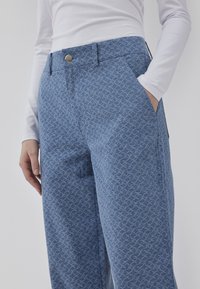 Light blue patterned trousers featuring a subtle design, high waist, front pockets, and a silver button fastener.