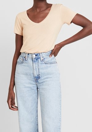 Licht perzikkleurig V-hals T-shirt gemaakt van zachte stof, gecombineerd met lichtblauwe denim jeans met hoge taille, subtiele vervaging en een losse pasvorm.