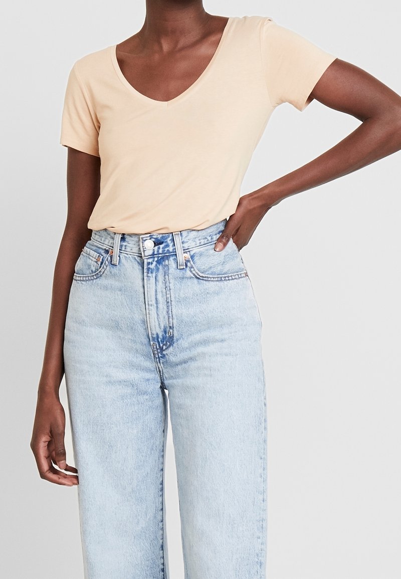 T-shirt à col en V couleur pêche clair en tissu doux, assorti à un jean en denim bleu clair taille haute avec un léger effet délavé et une coupe ample.