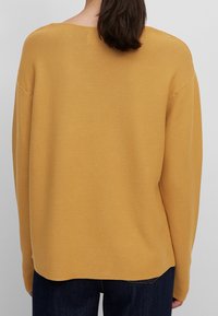 Maglione a coste di un giallo senape con una vestibilità comoda, scollatura ampia e texture a coste, abbinato a jeans in denim scuro.