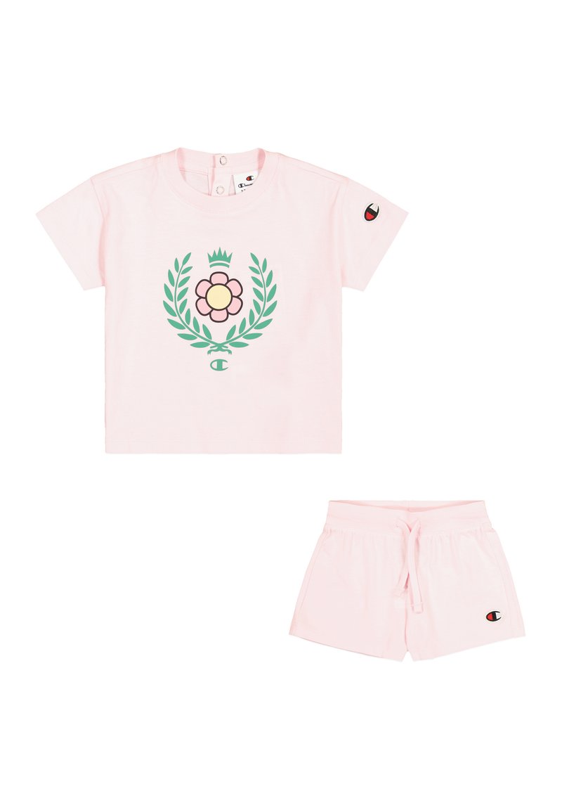 Camiseta corta de algodón rosa con un gráfico floral y hojas verdes, combinada con pantalones cortos rosa con cordón a juego. Incluye un parche de logo.