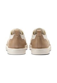 Pár béžových a bílých kožených bot s brogue detailem a bílými vroubkovanými podrážkami označenými "FLOWERFOAM", pohled zezadu.