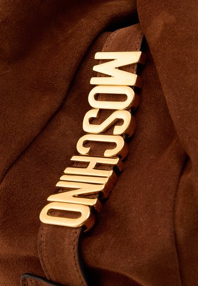 Καφέ σουέτ υλικό με σκούρο καφέ δερμάτινο λουράκι, με χρυσά μεταλλικά γράμματα που σχηματίζουν τη λέξη «MOSCHINO».