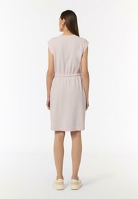 Helles rosa Kleid mit kurzen Ärmeln, tailliertem Schnitt und knielangem Saum, aus glattem Stoff, getragen mit beigen Sneakers.