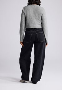 Szürke crop pulóver és sötétkék magasderekú, széles szárú farmernadrág, hátsó zsebekkel és kontrasztos varrással. Texturált fekete lábbelivel viselve.