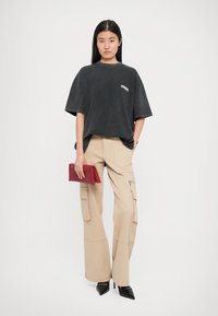 Camiseta de algodón negra de gran tamaño con mangas cortas, pantalones cargo beiges de pierna ancha y elegantes tacones negros puntiagudos. Bolso de mano de cuero rojo.
