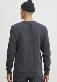 Felpa grigia scura con pannello a contrasto spalle, maniche lunghe, polsini a costine e scollatura rotonda. Tessuto morbido, design informale.