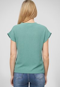 Grønn teksturert t-skjorte med korte ermer, rund hals og avslappet passform, kombinert med blå denimjeans.