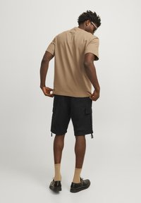 Brun kortærmet t-shirt parret med sorte cargo shorts, udsmykket med lommer og snore. Sorte sko og brune sokker fuldender looket.