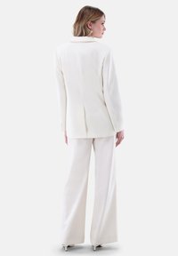 Weißer maßgeschneiderter Blazer mit langen Ärmeln und Revers, kombiniert mit weiten Hosen. Glattes Material mit einem klaren, minimalistischen Design.