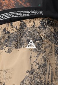 ACG Shorts in Beige mit schwarz inspirierter Grafik im Naturdesign. Mit einem elastischen Bund, Seitentasche und dreieckigem Logo-Patch.