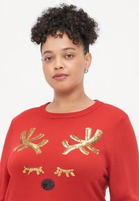 Sweater vermelho com chifres de rena em lantejoulas douradas e características faciais. Apresenta um decote arredondado e um tecido de malha texturizado.