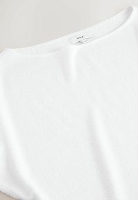 Haut en maille blanc uni avec un col rond et une étiquette de vêtement portant la mention NEXT à l'arrière.
