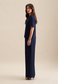Completo navy a due pezzi composto da una maglietta a maniche corte e pantaloni lunghi e dritti. Tessuto liscio e design minimalista con una silhouette vista di lato.
