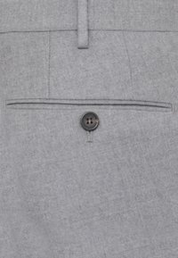 Primo piano di una tasca posteriore di un pantalone in tessuto grigio con un singolo bottone nero e un passante per cintura sopra.