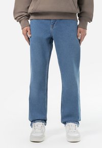 Ljust blå denimjeans med rak klippdesign, som har en klassisk femfickorstil och en subtilt blekt textur, tillsammans med vita sneakers.