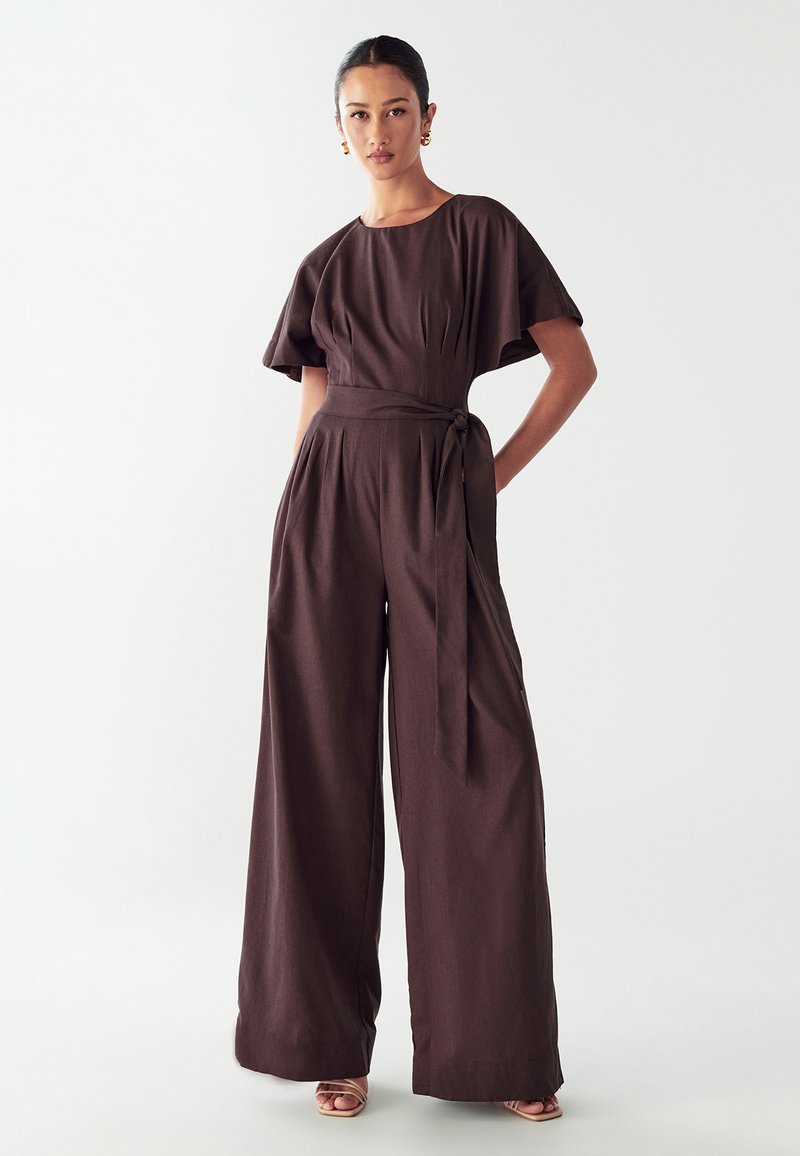 Mono marrón con mangas cortas, cinturón en la cintura y pantalones de pierna ancha. Textura de tela suave, diseño minimalista y color sólido.