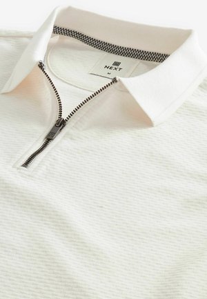 Polo bianco con un motivo testurizzato, chiusura con zip e interno del colletto a scacchi. L'etichetta riporta "NEXT" con la taglia "M."
