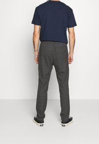 Gray plaid trousers with a relaxed fit, featuring a single back pocket, paired with a navy t-shirt and black sneakers.