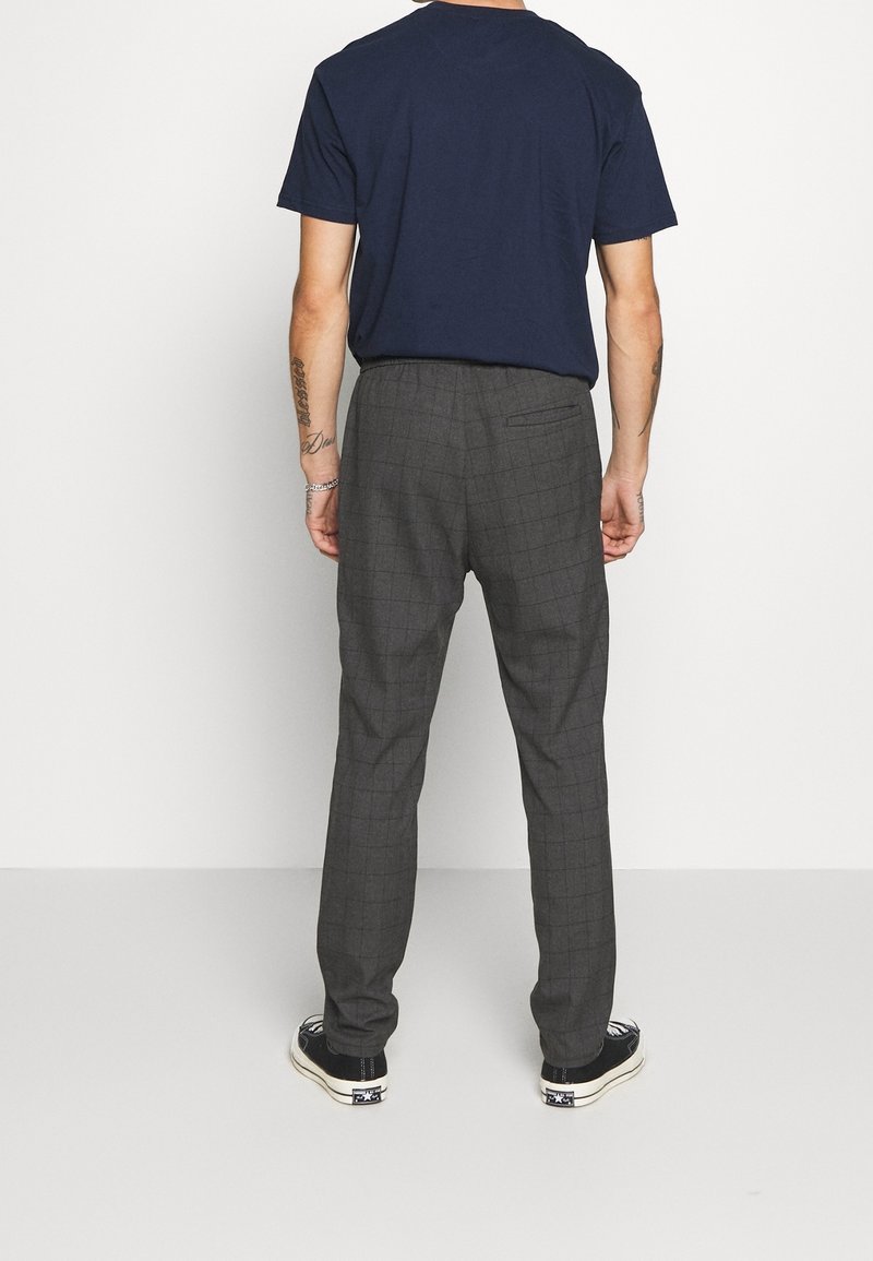 Gray plaid trousers with a relaxed fit, featuring a single back pocket, paired with a navy t-shirt and black sneakers.
