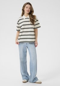 Polo à manches courtes avec des rayures noires sur un fond crème ; associé à un jean large bleu clair et des baskets beiges.