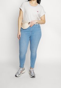 Stribet kortærmet t-shirt i hvid og lyseblå, parret med tætsiddende lyseblå jeans og metallisk sølvfarvede sneakers. Bæltepose omkring taljen.