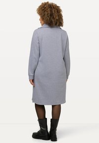 Vestido gris hasta la rodilla con mangas largas y cuello. Tejido texturizado, corte recto, combinado con botas de combate negras. Se muestra la vista trasera.