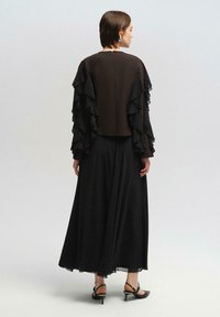 Juodas suknelė su sluoksniuotomis raukinėlių rankovėmis, plazdančiu sijonu ir kulkšnies ilgio dizainu. Lygus, lengvas audinys su užtrauktuku nugaroje.