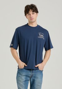 Navblå bomulds t-shirt med rund hals og korte ærmer, prydet med et hvidt grafiktryk på brystet og et logodetalje på ærmet.