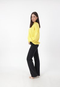 Maglione giallo lavorato a maglia con una vestibilità ampia e polsini a coste, abbinato a jeans neri a vita alta e zeppe trasparenti.
