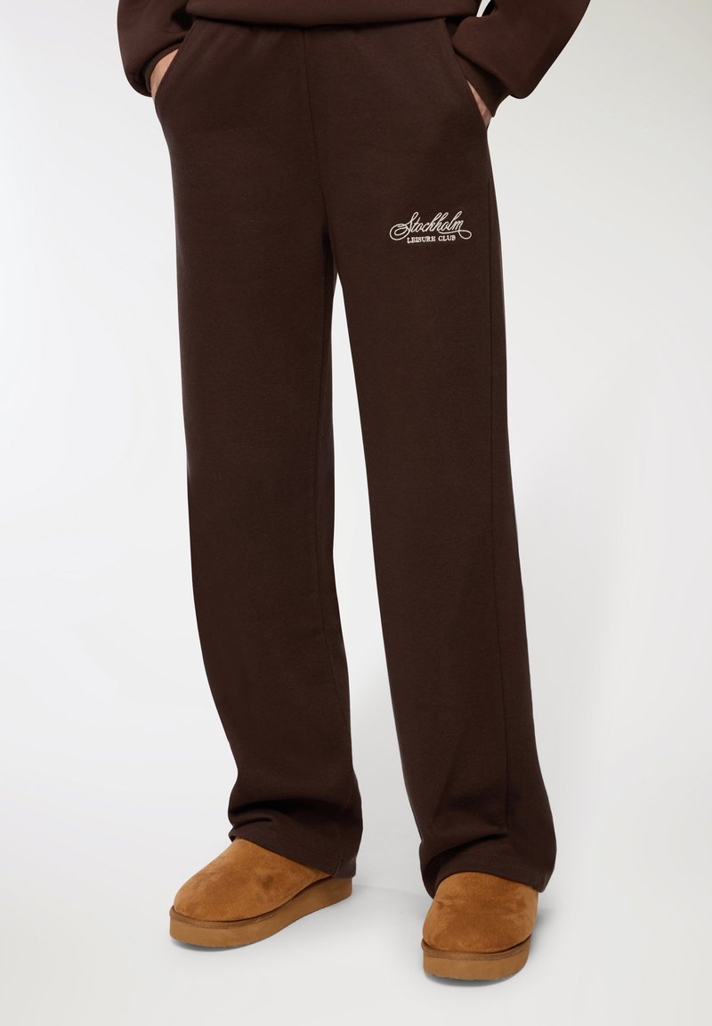 Brązowe dresy wykonane z miękkiego materiału, w luźnym kroju, z bocznymi kieszeniami i haftem 'Stockholm Leisure Club' na udzie.