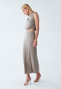 Beige todelt tøj bestående af en cropped, ærmeløs top med en rund halsudskæring og en lang, slank nederdel. Glat, skinnende stof med tætsiddende design.