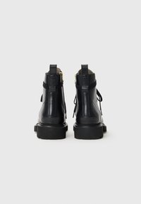 Bottes noires en cuir avec une semelle épaisse, fermeture éclair sur le côté et lacets décoratifs. Texture lisse avec des détails matériels minimaux.