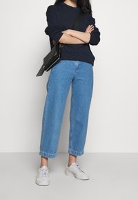 Outfit casual composto da un felpa navy, jeans di denim a gamba larga azzurri e sneakers bianche. La borsa nera aggiunge un dettaglio a contrasto.