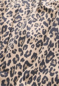 Tela beige con un estampado de leopardo negro y gris, mostrando pliegues suaves y textura del material de punto.