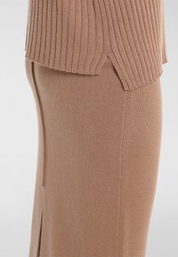 Pull en maille côtelée marron avec fentes latérales, associé à une jupe marron lisse et ajustée. Les deux pièces présentent une texture douce et un design épuré.